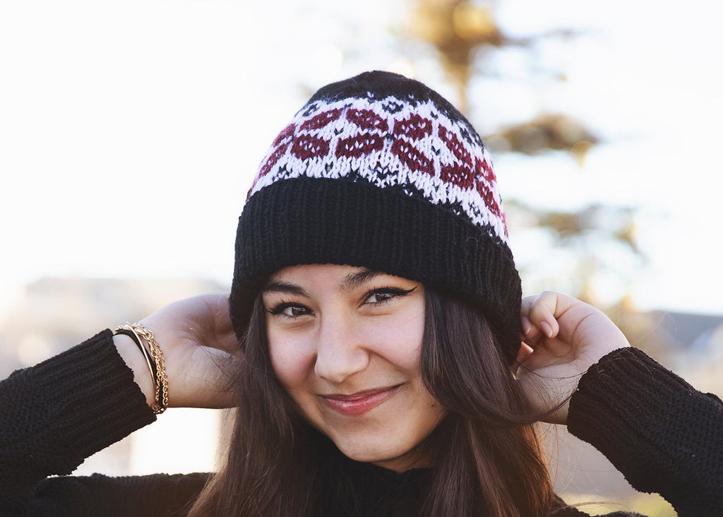 Woman wearing a black knit beanie with a pattern, smiling outdoors.