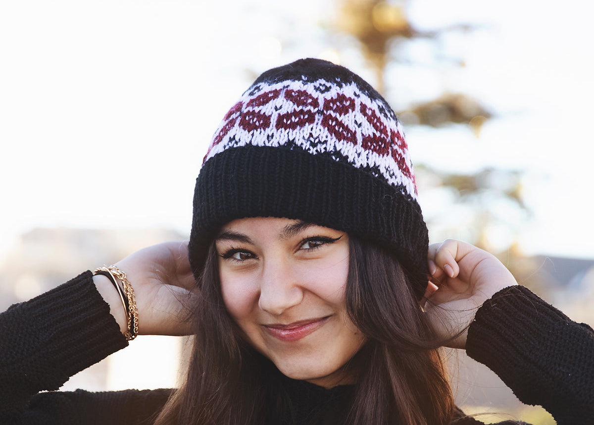 Woman wearing a black knit beanie with a pattern, smiling outdoors.
